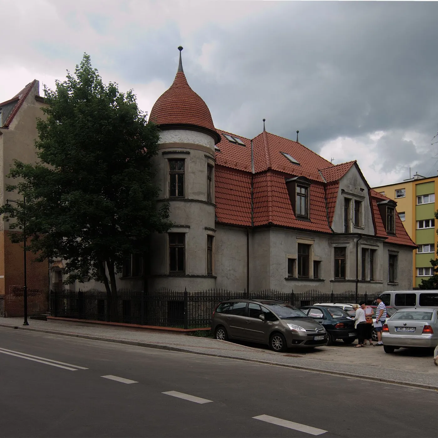 Dom przy ulicy Armii Krajowej 15 z okrągłą wieżyczką z iglicą i czerwonym dachem z lukarnami.