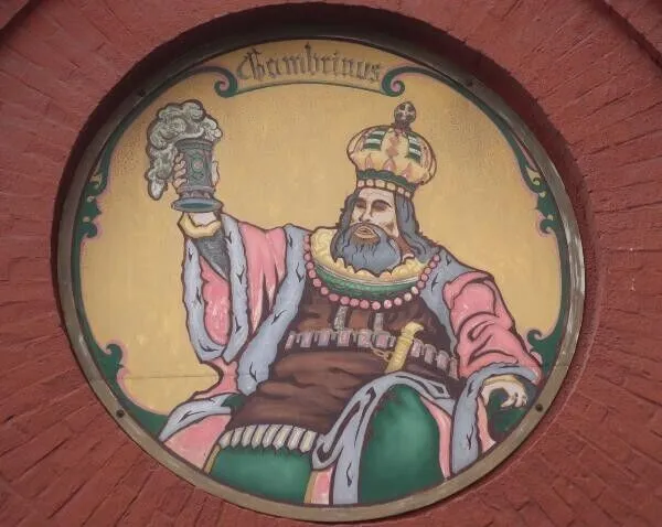 Okrągły malowany medalion na ceglanej ścianie: Gambrinus w koronie z kuflem piwa.