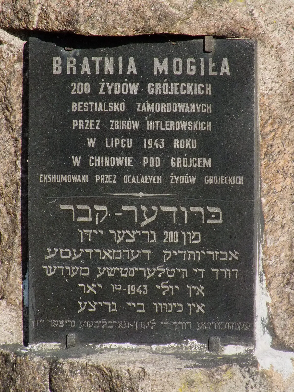 Czarna tablica na kamiennym pomniku na cmentarzu żydowskim w Grójcu, z napisem po polsku i w jidysz o bratniej mogile 200 grójeckich Żydów zamordowanych w 1943 roku.