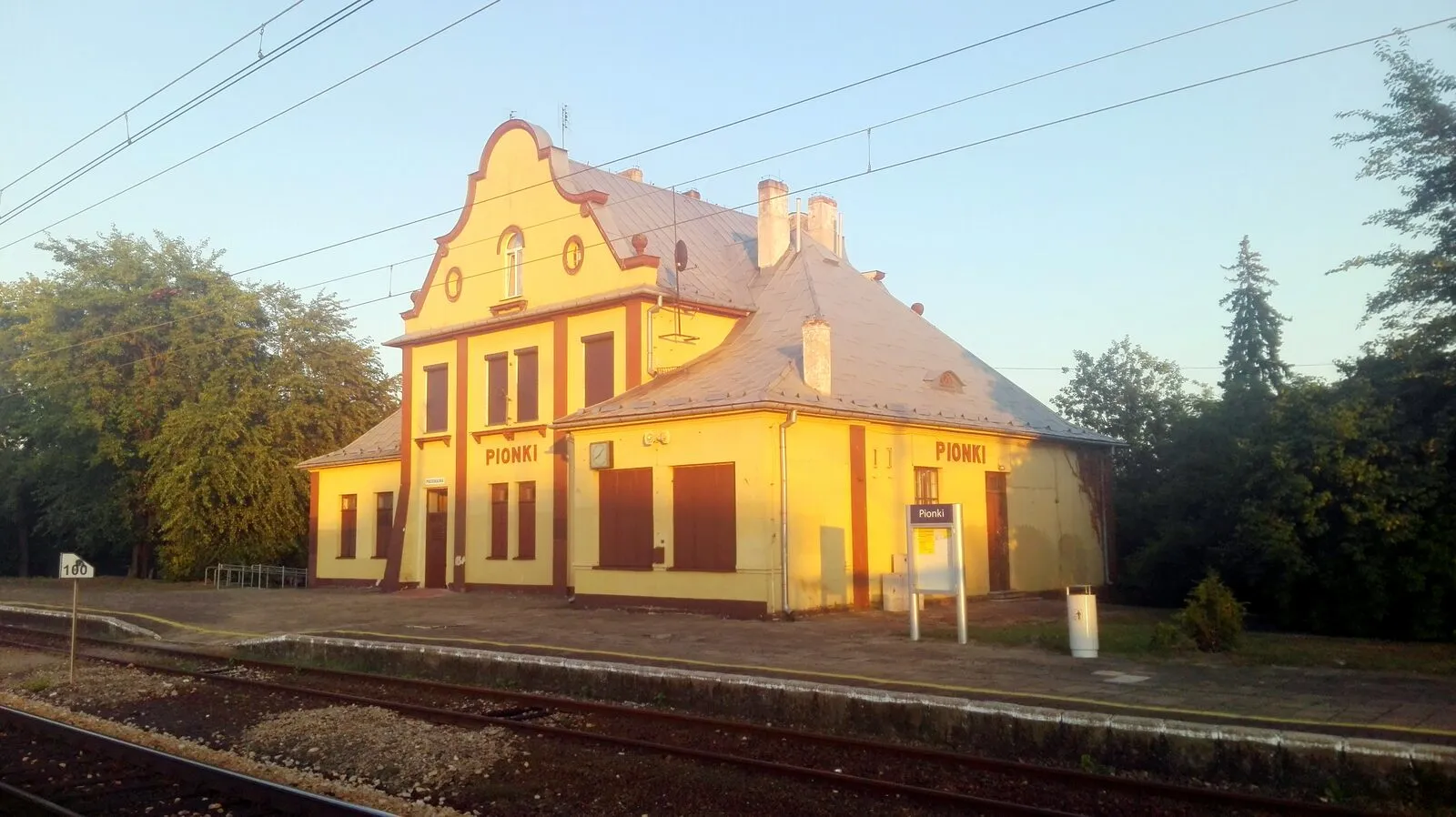 Dworzec kolejowy w Pionkach o zachodzie słońca, budynek w stylu dworkowym widziany od torów