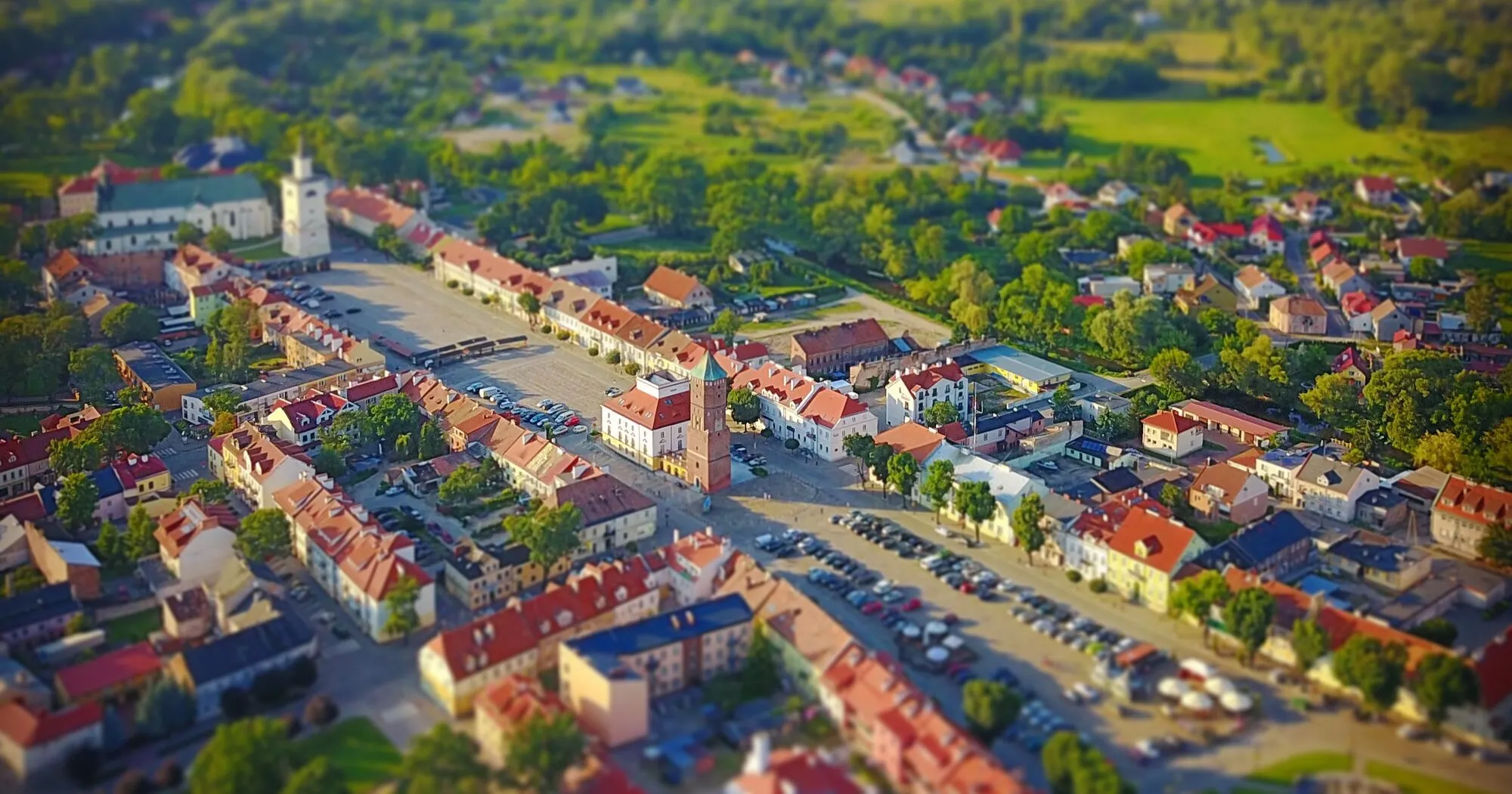 Rynek w Pułtusku z lotu ptaka: długi plac z ratuszową wieżą, czerwone dachy kamienic i zielone okolice miasta