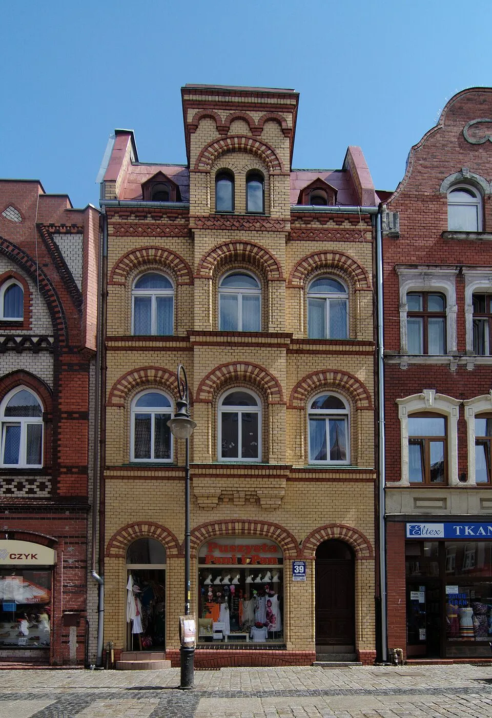 Wąska kamienica przy ulicy Staromiejskiej 39 z żółtej i brunatnej cegły, z rzędami ceglanych łuków na fasadzie.