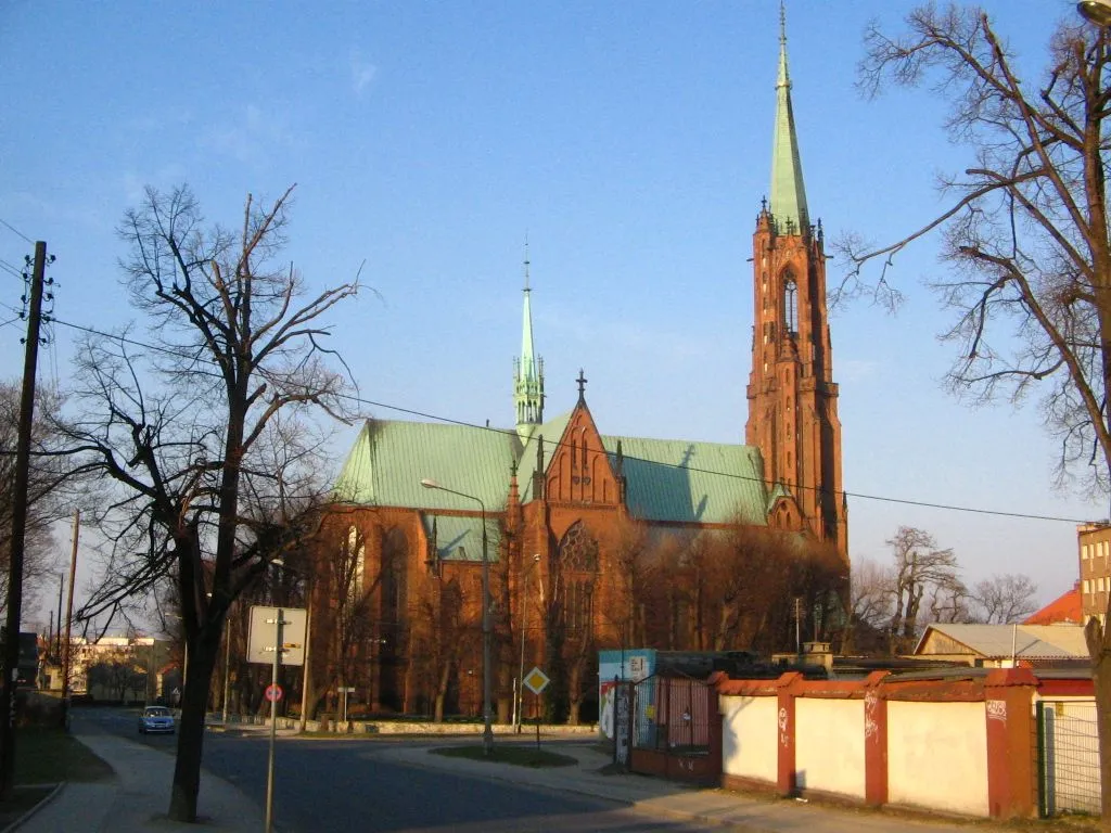 Ceglany kościół Wniebowzięcia NMP w Bielawie widziany z ulicy: wysoka wieża od frontu i mniejsza wieżyczka nad dachem.