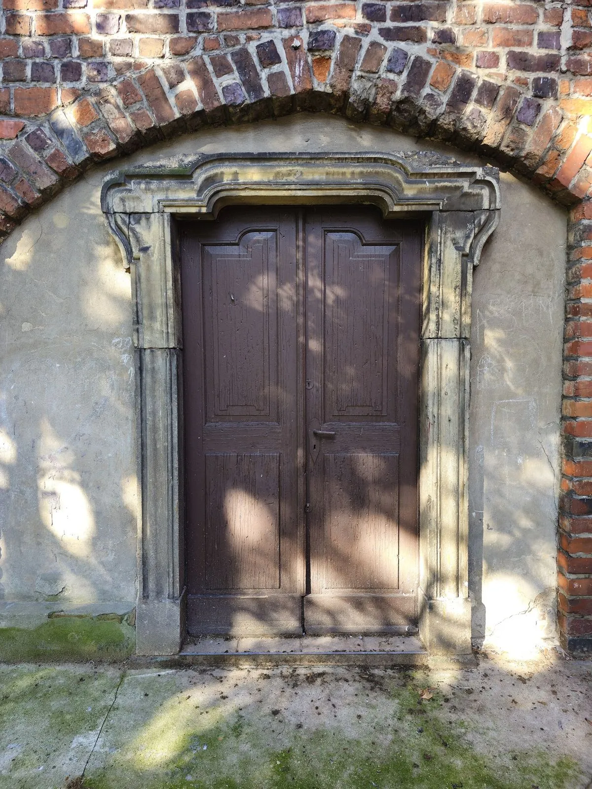 Kamienny portal z drewnianymi drzwiami w ceglanej ścianie dawnej synagogi