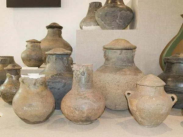Gliniane popielnice z pokrywkami, jedna z uformowaną twarzą, na wystawie archeologicznej.