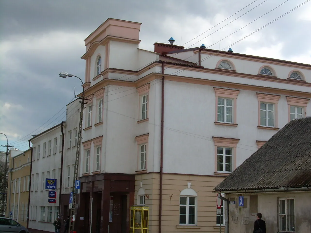 Neoklasycystyczny gmach dawnej poczty przy Grodzkiej 1 w Ciechanowie, z zaokrąglonym narożnikiem obejmującym zbieg ulic.