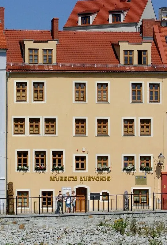 Jasna kamienica przy ulicy Daszyńskiego 15 w Zgorzelcu z napisem Muzeum Łużyckie na fasadzie i czerwonym dachem z lukarnami.