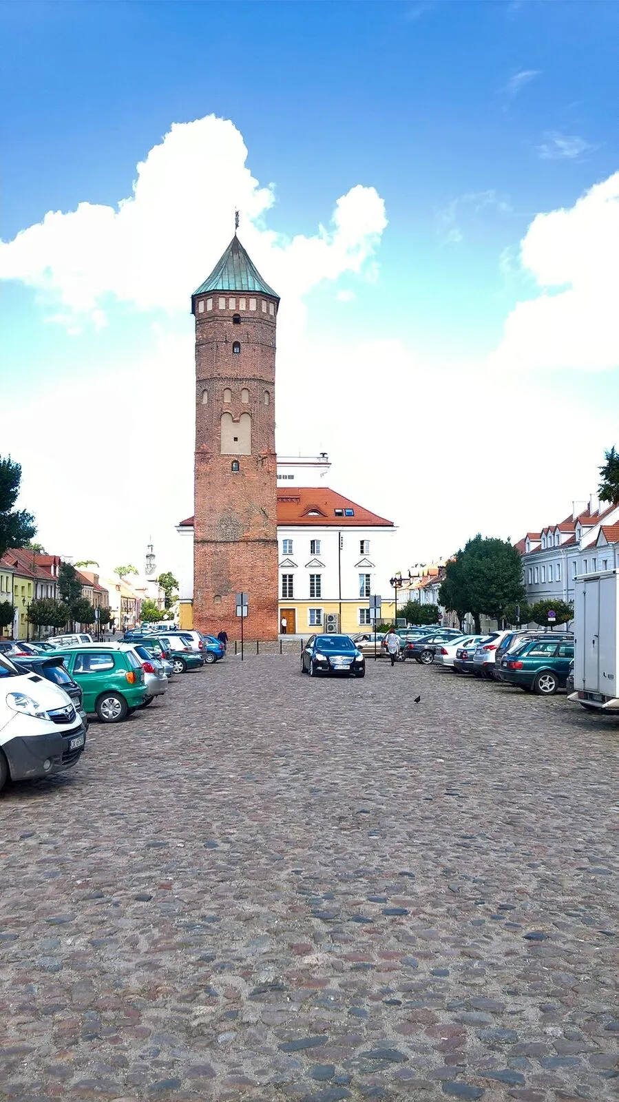 Gotycka ceglana wieża ratuszowa pośrodku długiego brukowanego rynku w Pułtusku.