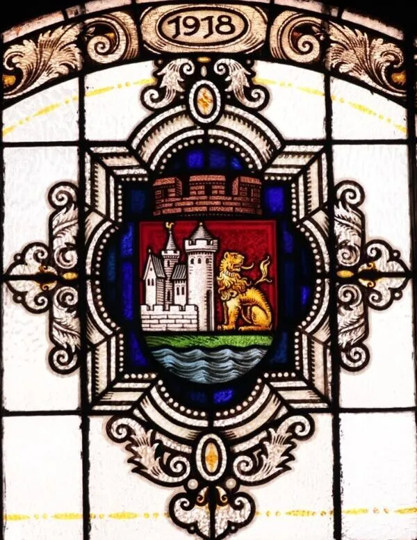 Witraż z herbem Lęborka w ozdobnej ramie z roślinnym ornamentem.