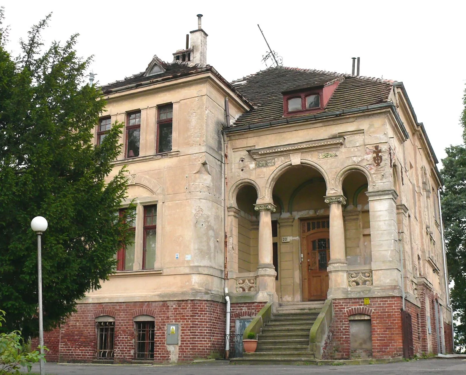 Jasna willa przy ulicy św. Jana 20 w Zgorzelcu z gankiem na kolumnach, schodami prowadzącymi do wejścia i wysokim dachem.