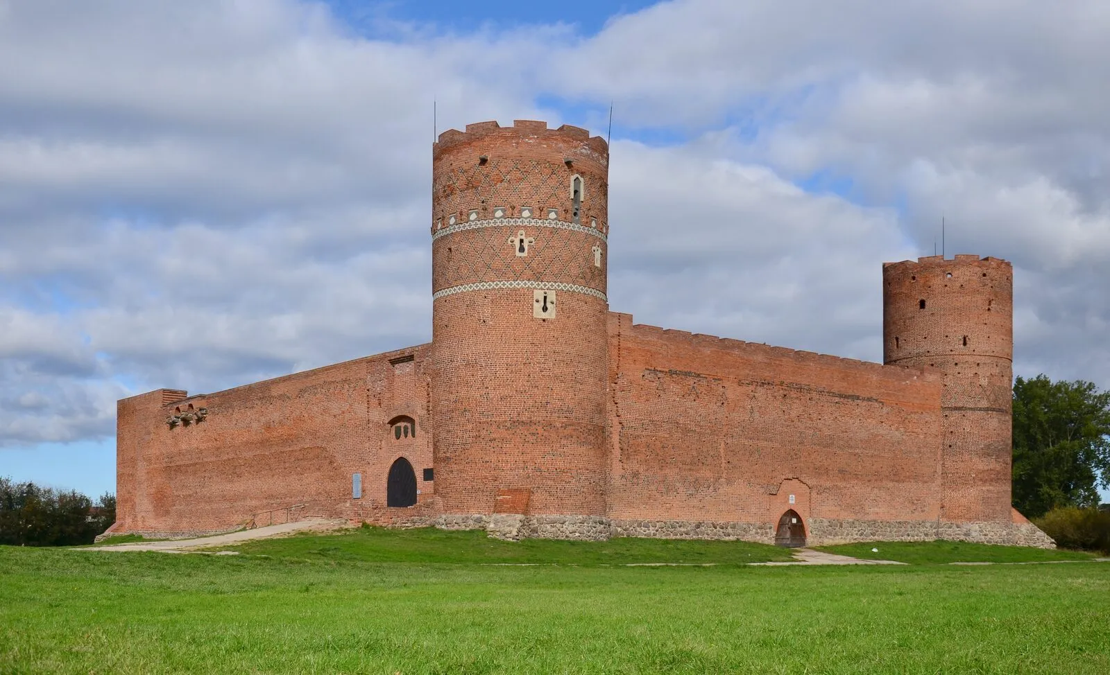 Gotycki zamek książąt mazowieckich w Ciechanowie: ceglane mury obronne z dwiema cylindrycznymi wieżami, na płaskim terenie nad Łydynią.