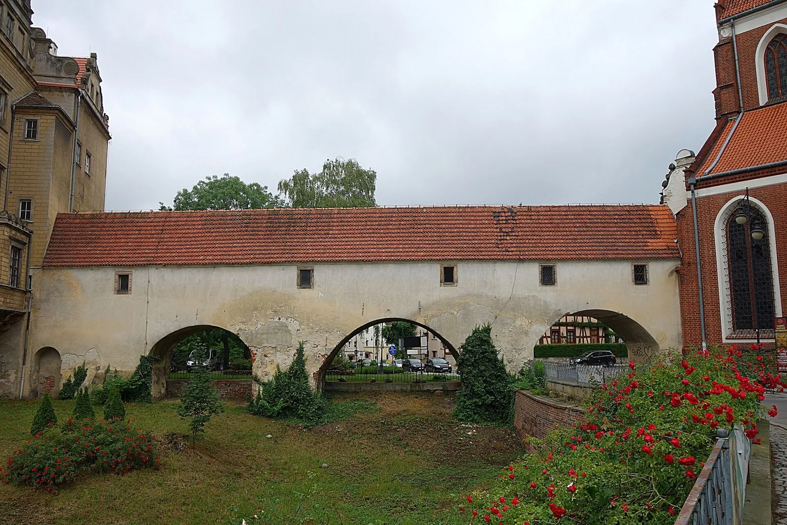 Kryty ganek wsparty na trzech łukach nad fosą, prowadzący do kościoła